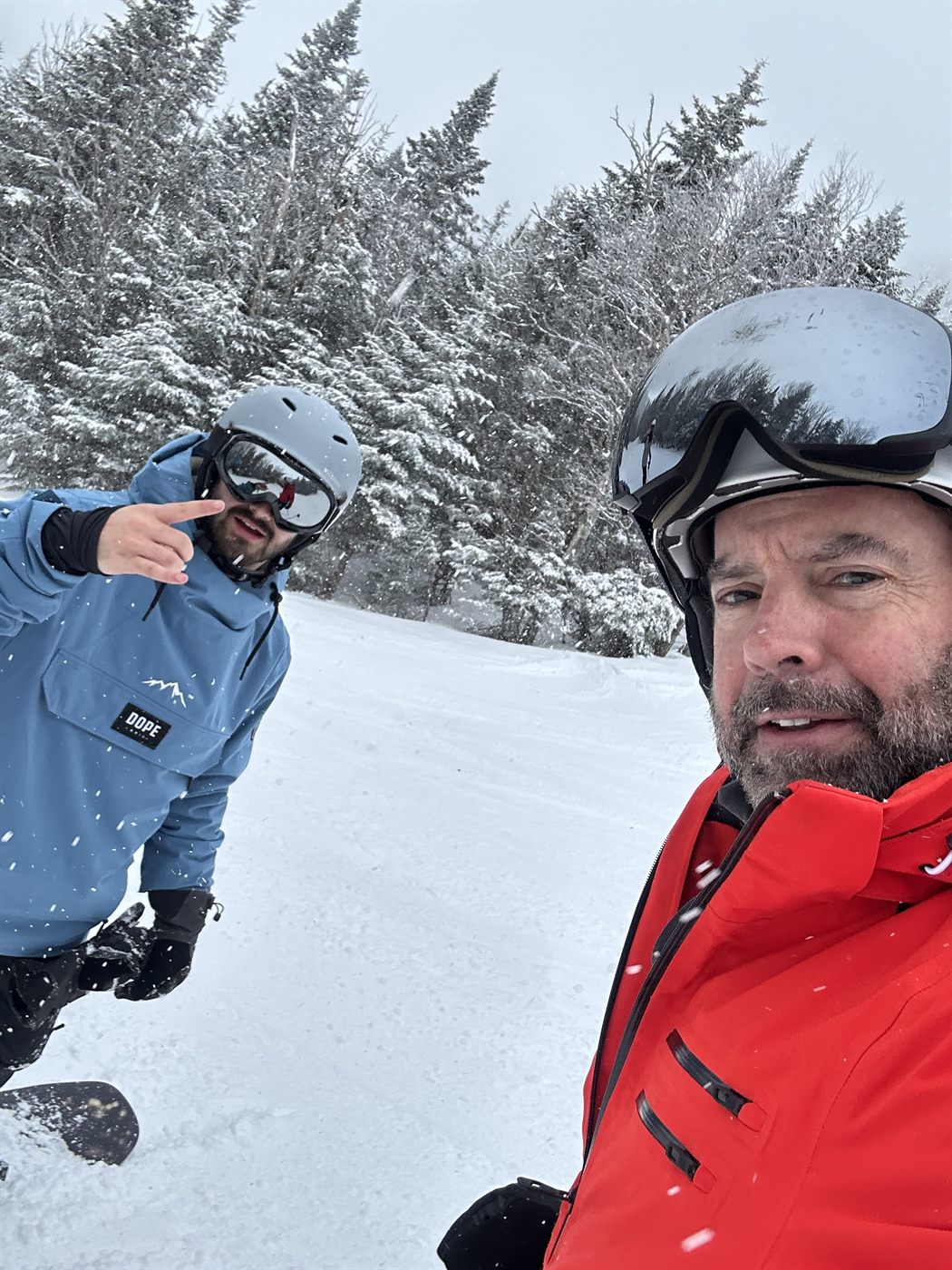 Gabe on a snowboard pointing at the camera in heavy snow while his dad takes the photo